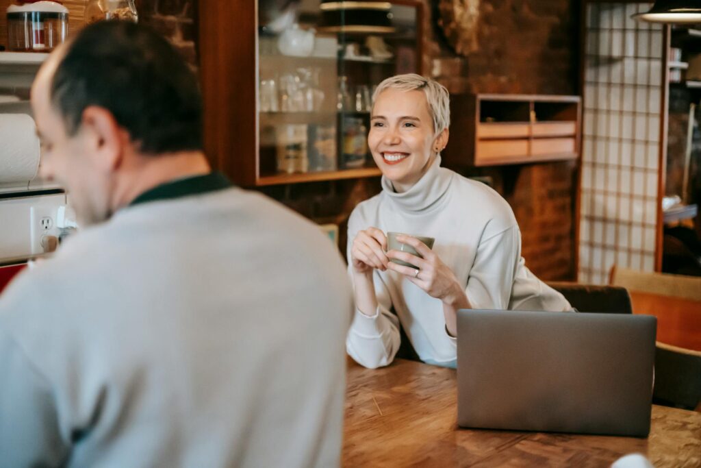 A cheerful couple having coffee and conversation in a cozy indoor setting, with a laptop on the table.