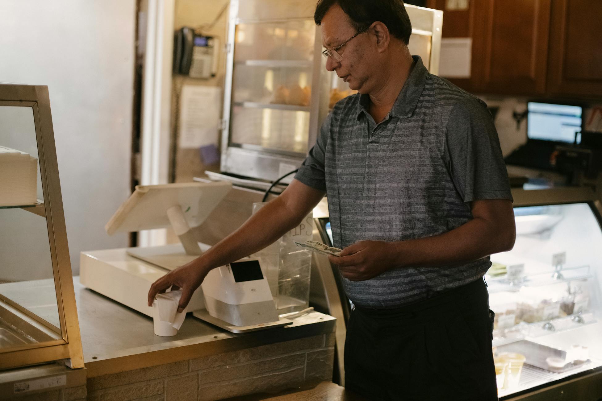 A man paying for a coffee at a café counter, holding cash. Indoor modern setting.