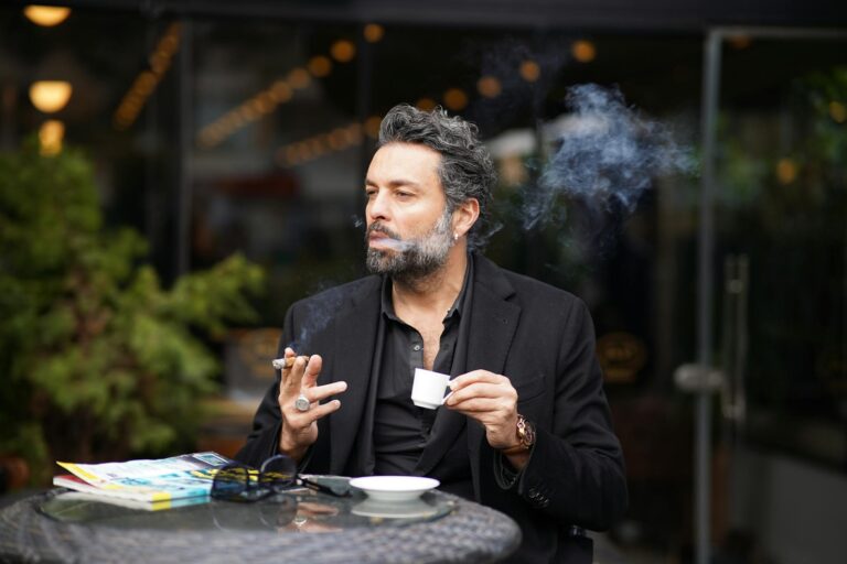 Middle-aged man enjoying a cigarette and coffee at an outdoor cafe.