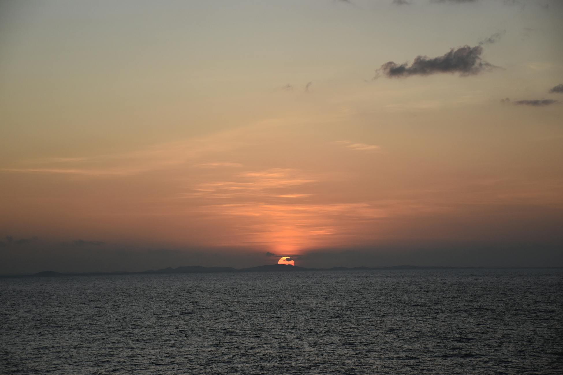 Beautiful sunset over a calm ocean with vibrant colors and distant land silhouette.