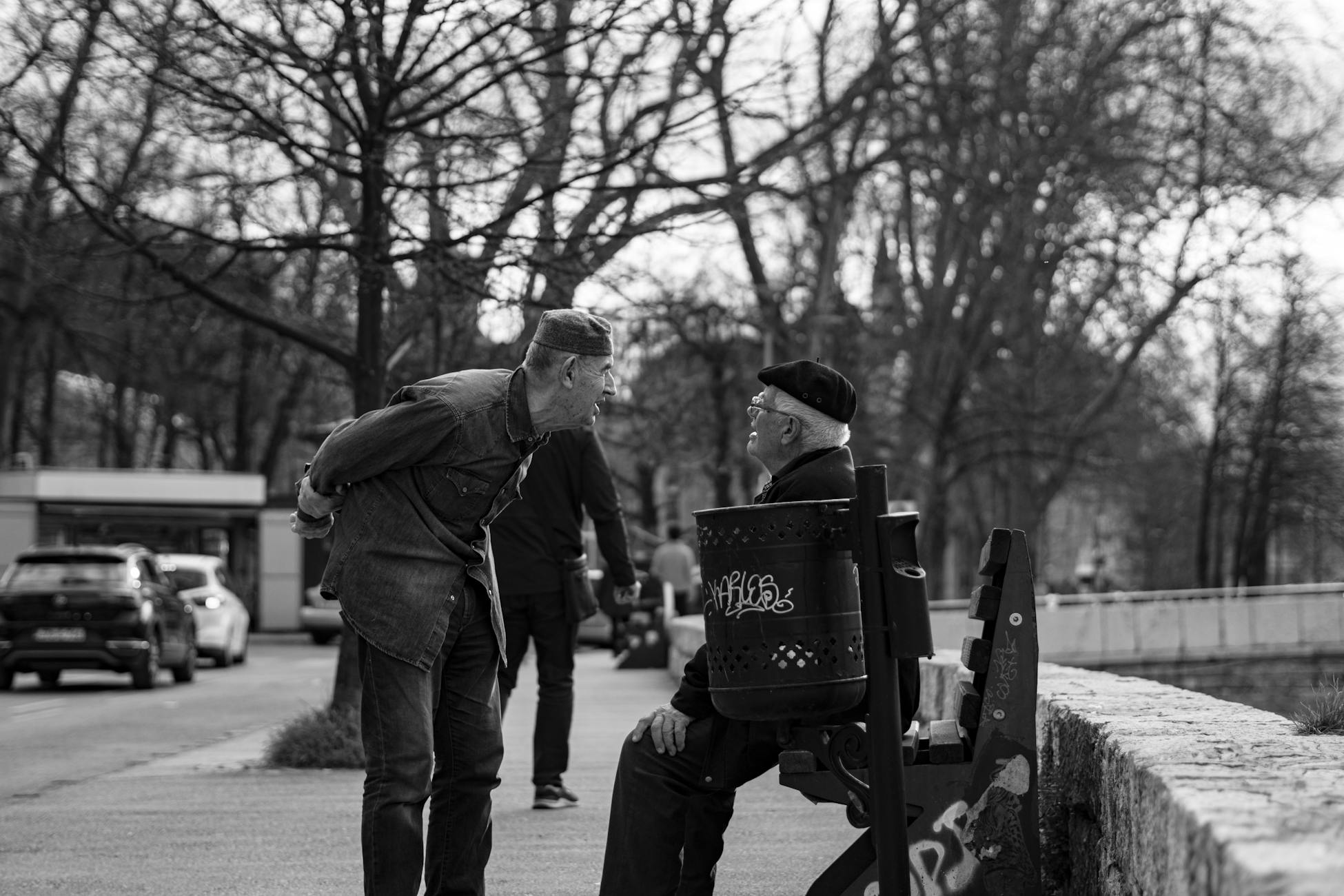 Two senior men engaging in conversation on a city bench, captured in black and white.