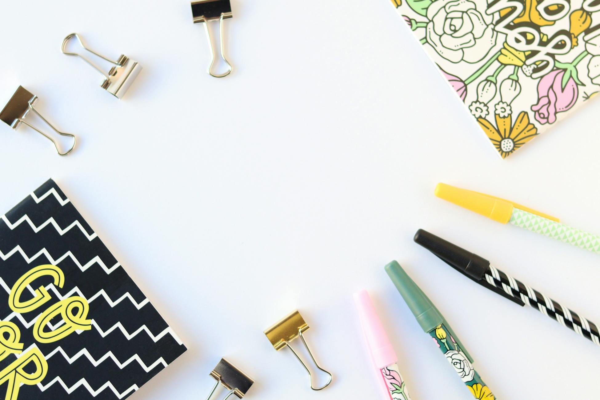 Vibrant flatlay of stationery including pens, notebooks, and clips on a white background.