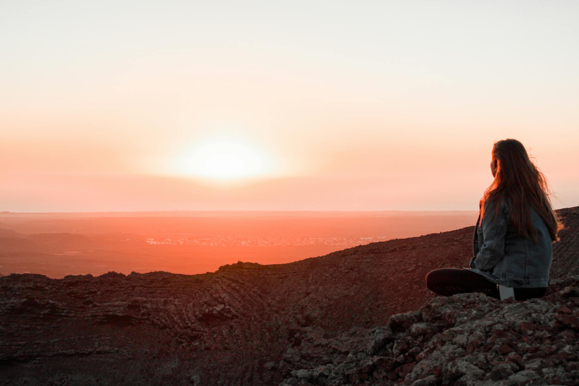 A woman sitting on a rocky mountain top in La Oliva, Canarias, enjoying a serene sunset view.