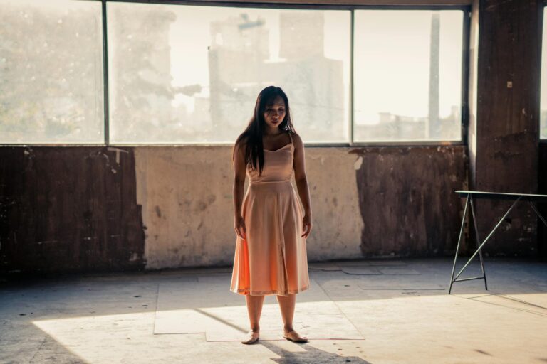 A solitary woman stands in an empty, sunlit room, conveying a sense of loneliness and introspection.
