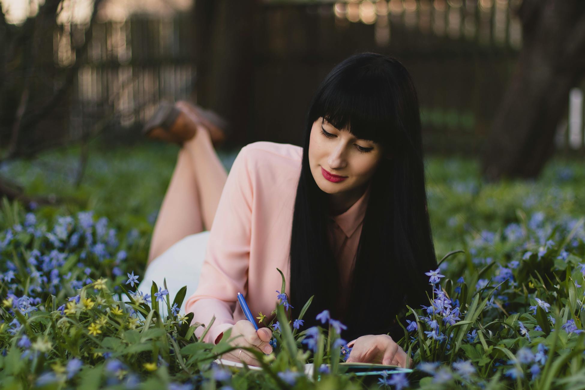 A woman writing in a journal while lying in a field of purple and yellow flowers outdoors.