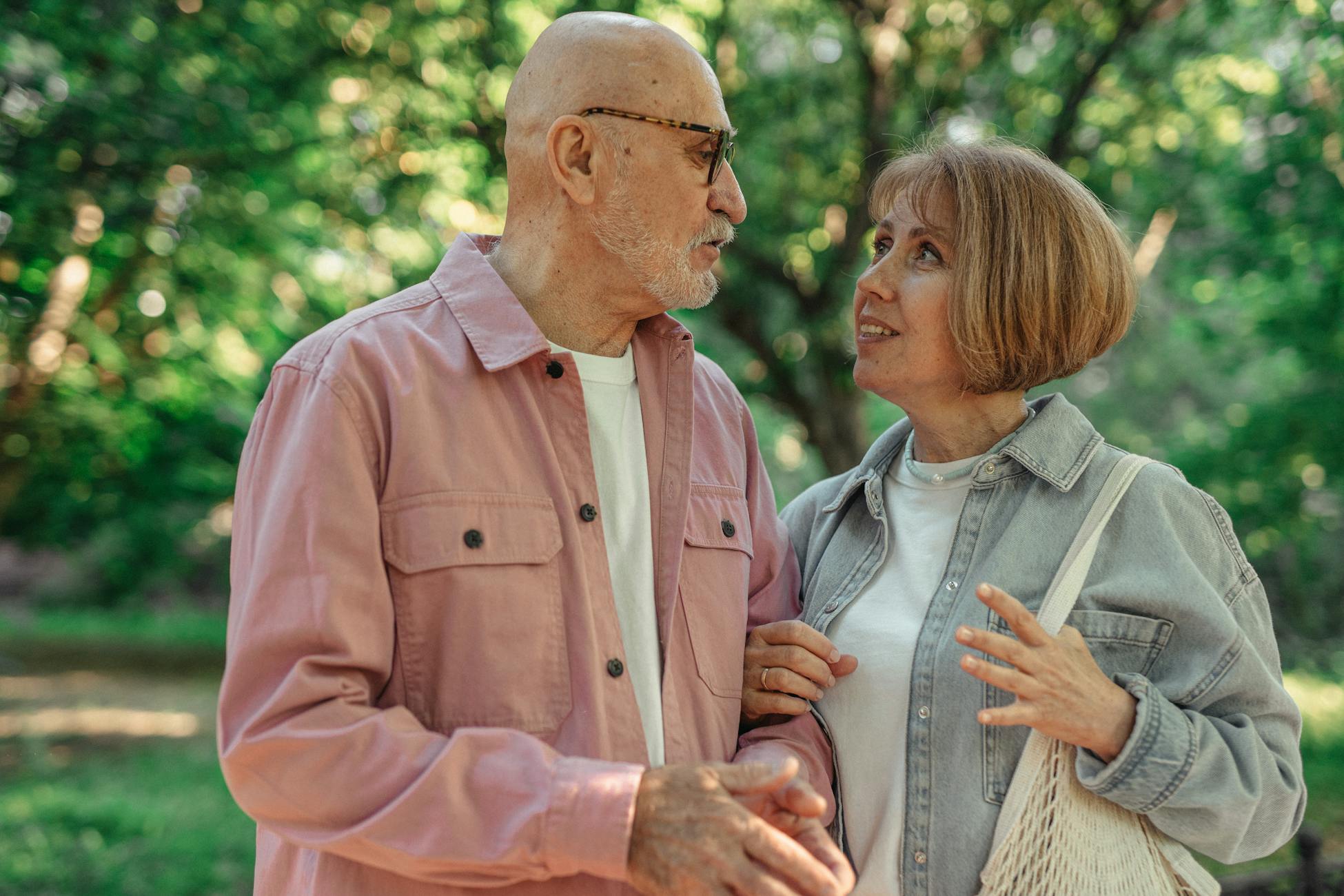 An elderly couple shares a joyful conversation in a vibrant green park setting.