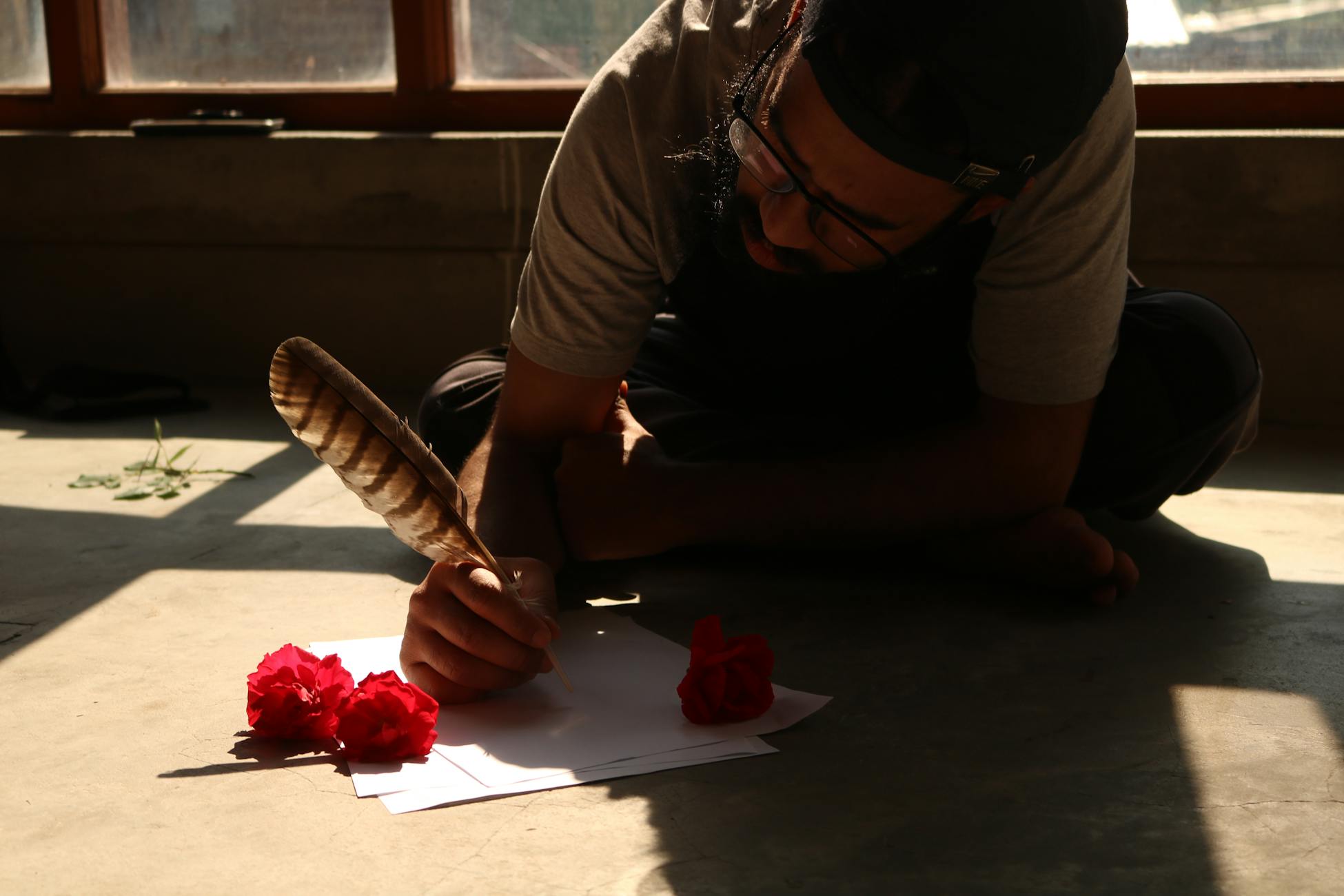 A man writing with a feather quill surrounded by red flowers, embodying creativity and concentration.