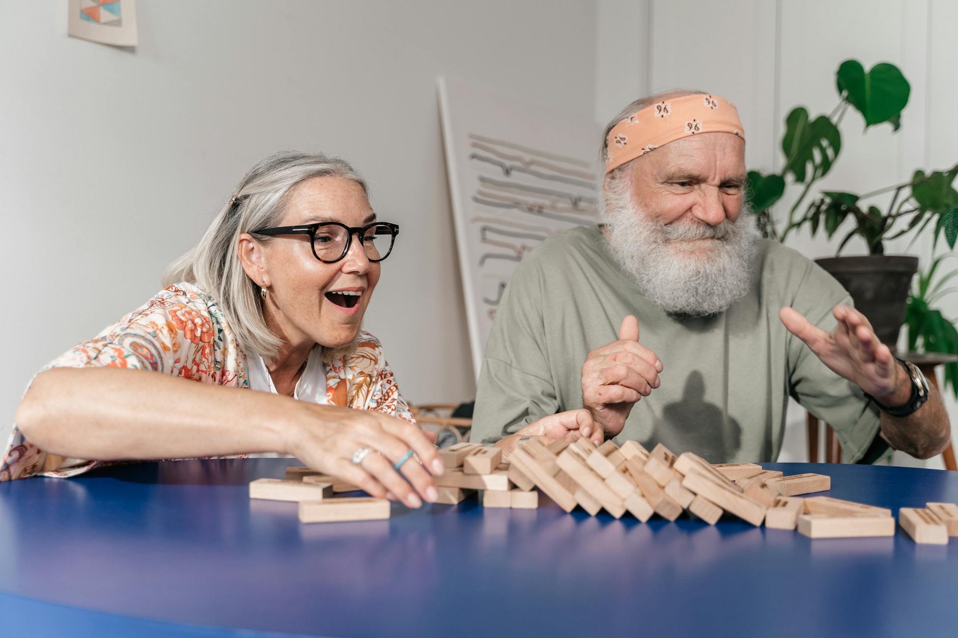 Elderly couple laughing and bonding while playing Jenga indoors.