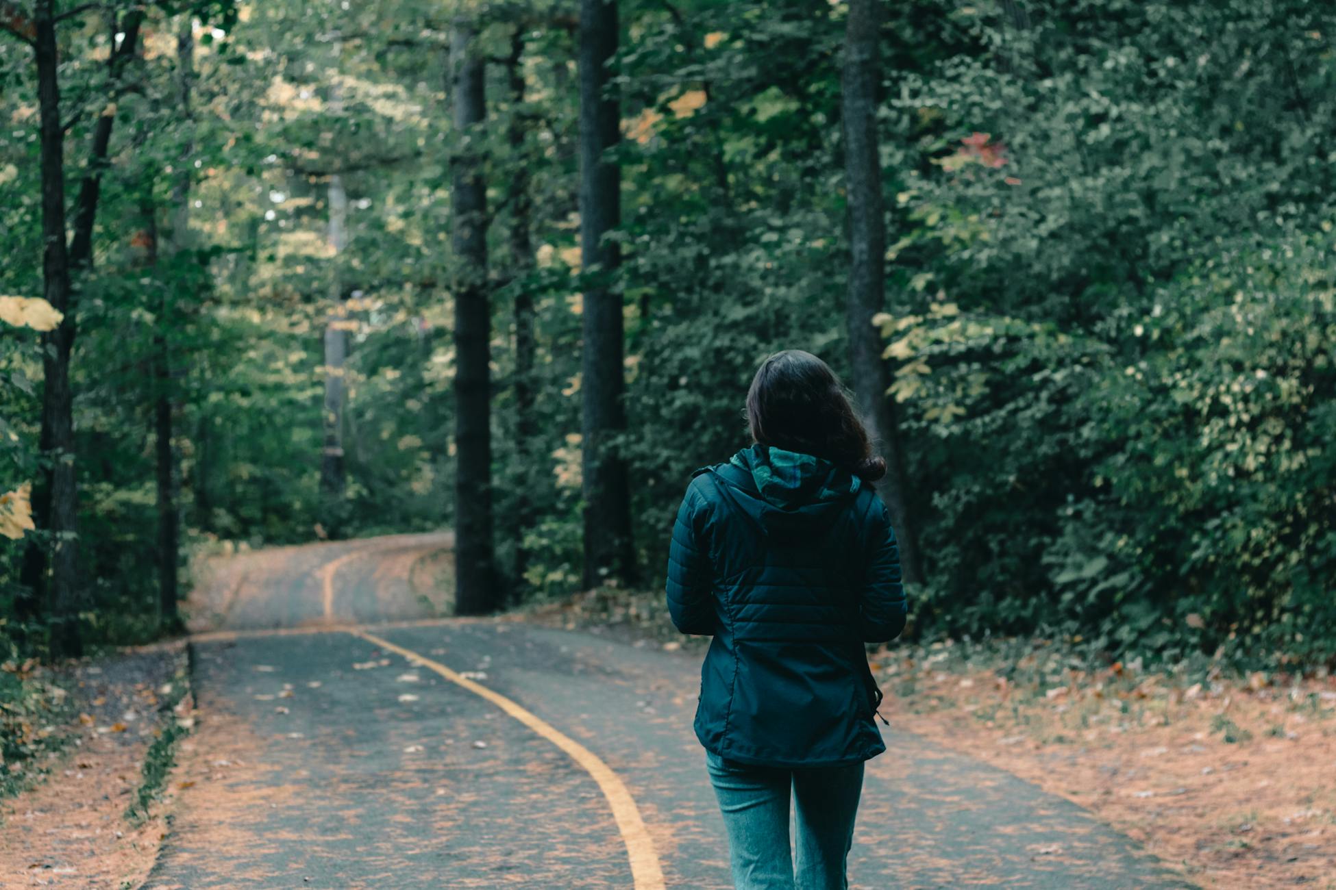 Rear view of a woman walking through a lush Canadian forest path during fall.