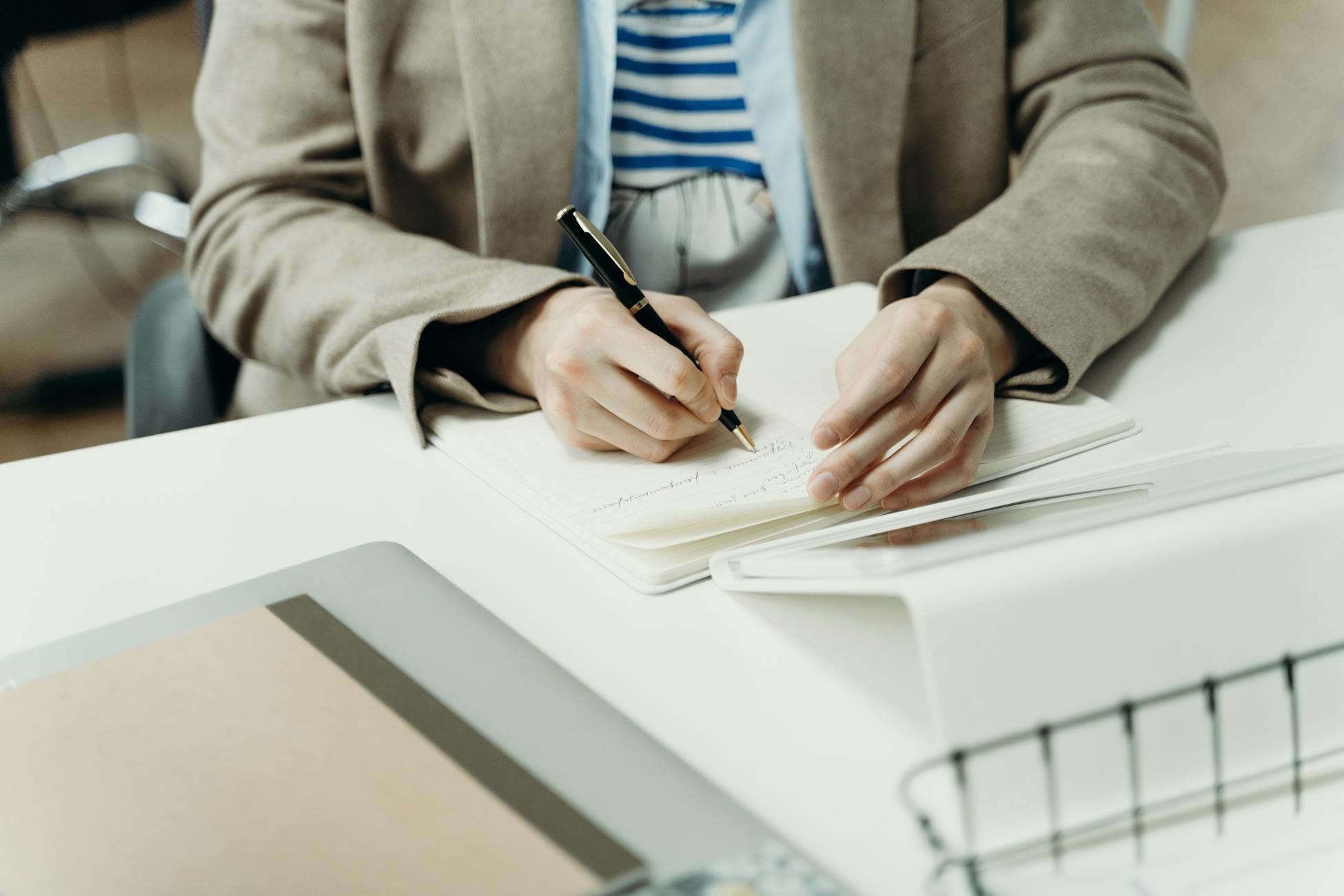 Close-up of an adult writing in a notebook at a modern office desk, capturing professional planning.