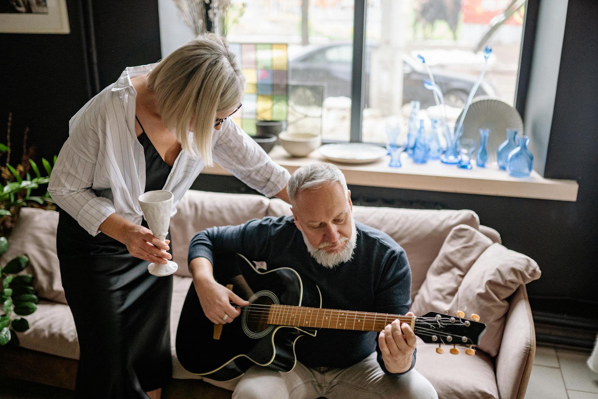 An elderly couple enjoys music indoors with a guitar and cozy decor.