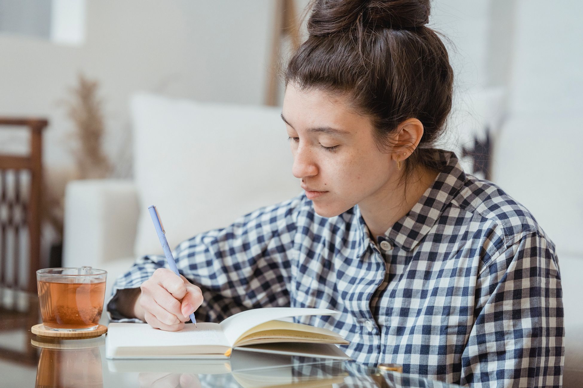 A young woman studying and writing in a notebook with a cup of tea nearby.